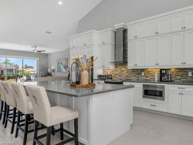Kitchen featuring backsplash, dark countertops, wall chimney range hood, a breakfast bar area, and appliances with stainless steel finishes