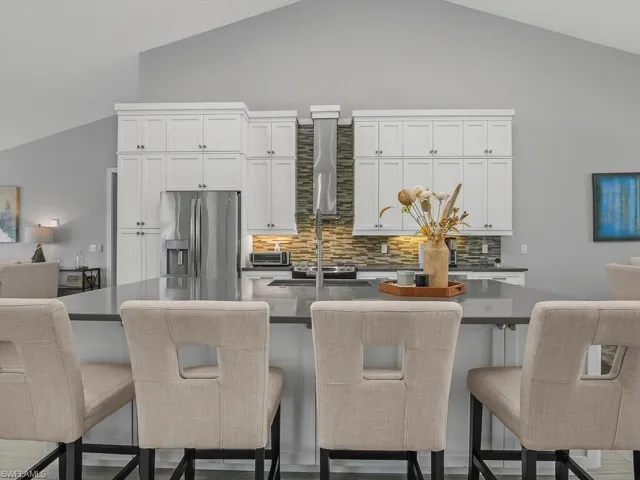 Kitchen featuring tasteful backsplash, stainless steel fridge with ice dispenser, white cabinets, an island with sink, and wall chimney exhaust hood