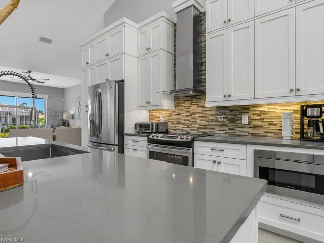 Kitchen featuring wall chimney range hood, stainless steel appliances, backsplash, white cabinets, and vaulted ceiling