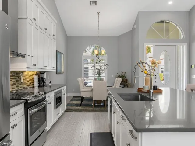 Kitchen featuring dark countertops, a center island with sink, stainless steel appliances, a chandelier, and tasteful backsplash