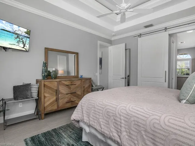 Bedroom featuring a barn door, crown molding, ceiling fan, and a tray ceiling
