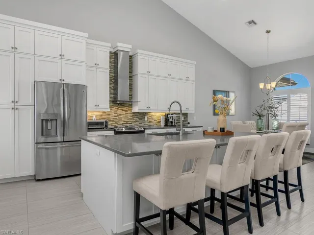 Kitchen with appliances with stainless steel finishes, backsplash, high vaulted ceiling, an island with sink, and a chandelier