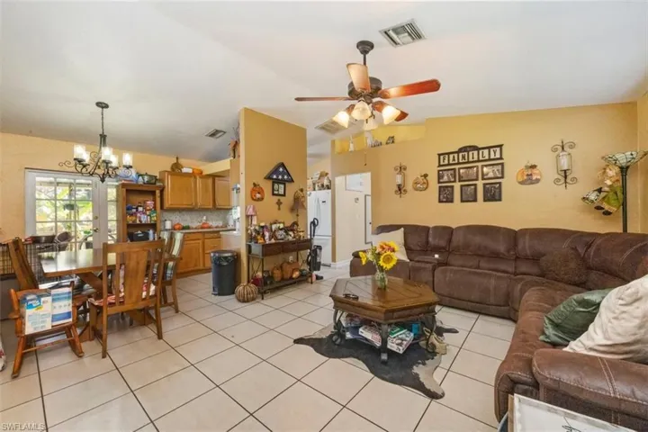 Living room with a ceiling fan, vaulted ceiling, light tile patterned floors, and a chandelier
