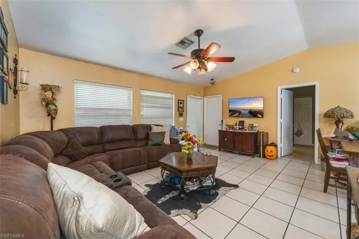 Living area with lofted ceiling, light tile patterned floors, and ceiling fan