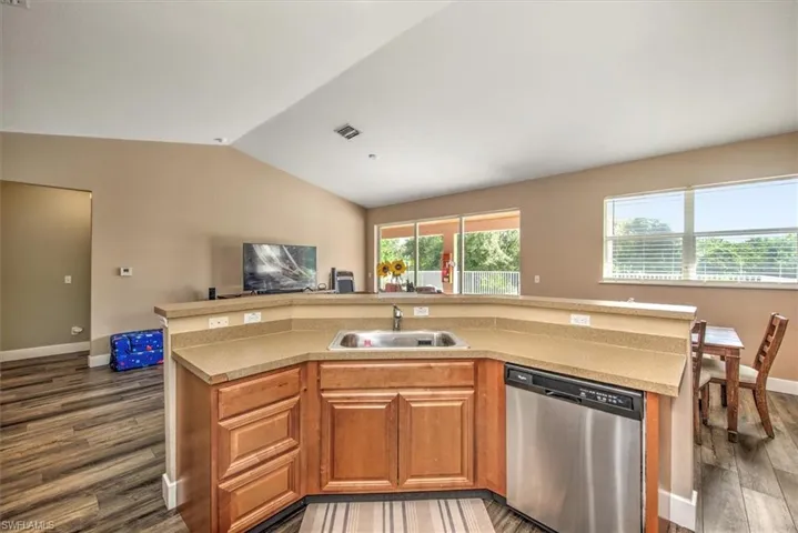 Kitchen featuring an island with sink, dark wood-type flooring, sink, vaulted ceiling, and dishwasher