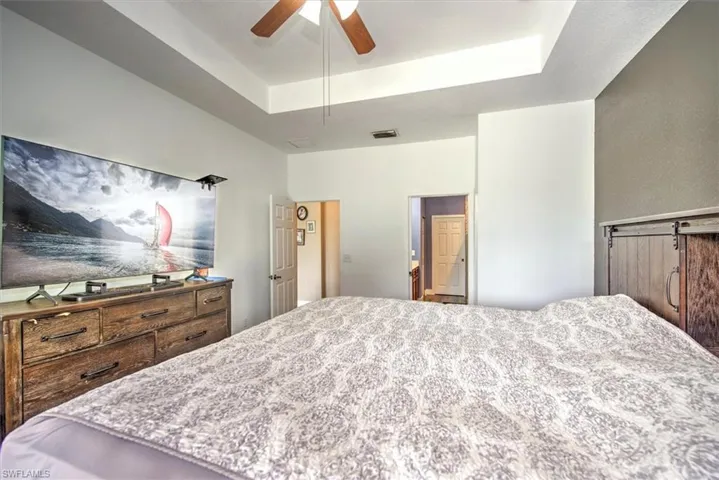 Bedroom featuring ceiling fan, a barn door, and a tray ceiling
