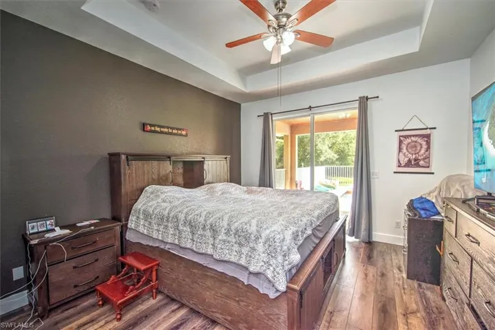 Bedroom with a tray ceiling, access to exterior, dark hardwood / wood-style flooring, and ceiling fan