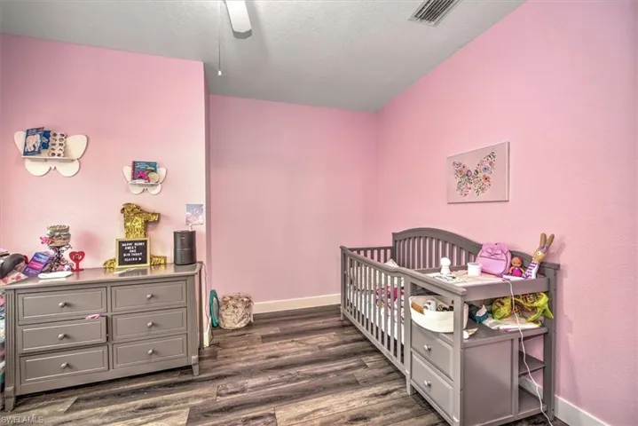 Bedroom featuring dark wood-type flooring, a nursery area, and ceiling fan