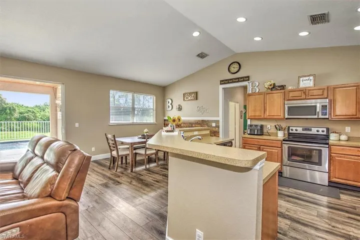 Kitchen with wood-type flooring, appliances with stainless steel finishes, lofted ceiling, and a healthy amount of sunlight