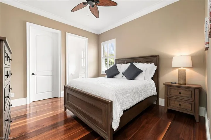 Guest bedroom with ensuite bathroom, ornamental molding, hardwood flooring, and ceiling fan