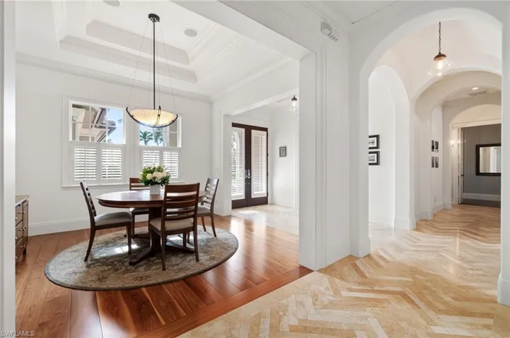 Dining space with hardwood flooring, a raised tray ceiling, glass entry doors, and herringbone Travertine tile leading to Primary ensuite