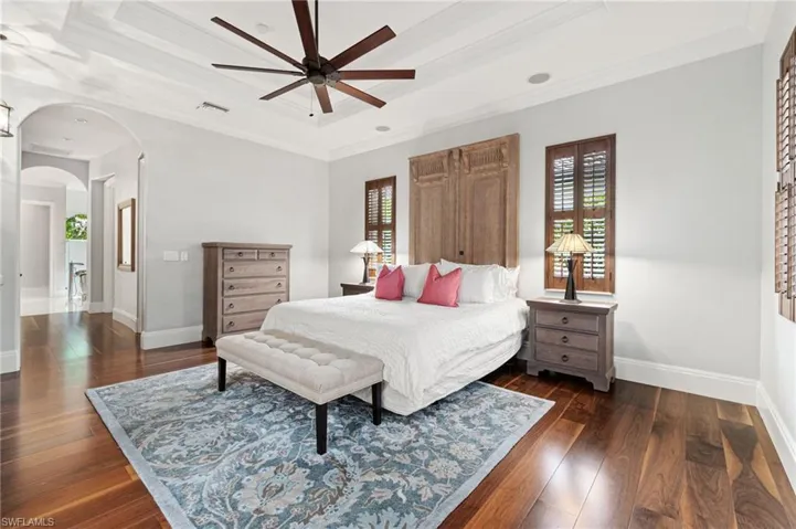 Primary ensuite bedroom with ornamental molding, ceiling fan, a tray ceiling, hardwood flooring