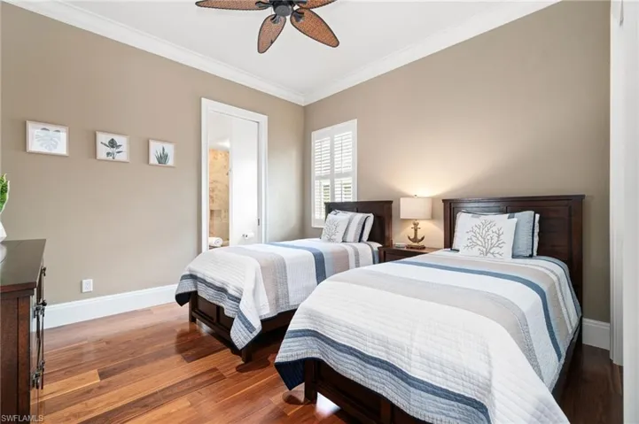 Guest bedroom with ensuite bathroom, hardwood flooring, and crown molding