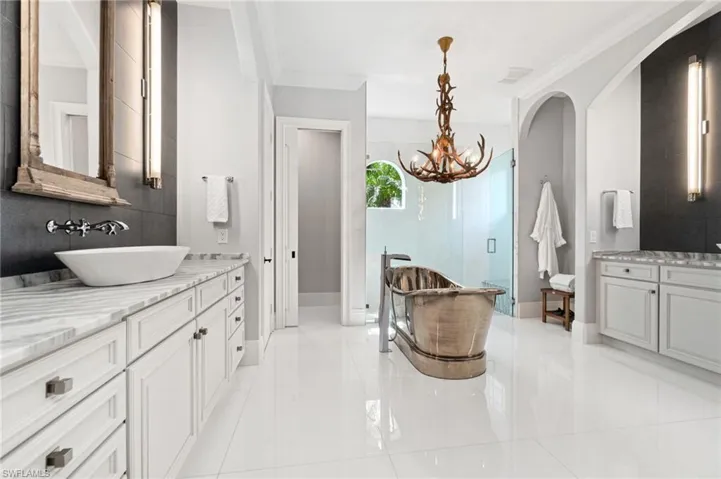 Bathroom with a custom chandelier, walk in glass shower, dual vanities, linen closet