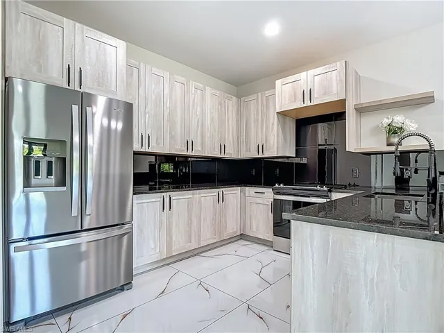 Kitchen with stainless steel appliances, open shelves, dark stone counters, decorative backsplash, and light marble finish flooring