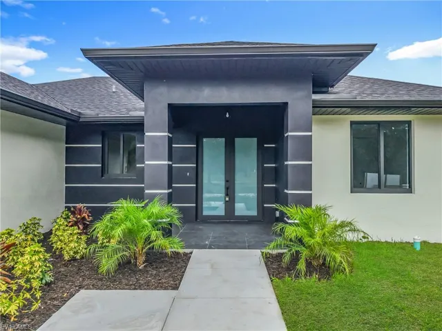 View of exterior entry with roof with shingles, stucco siding, french doors, and a yard