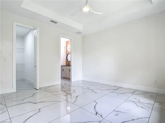 Empty room with light marble finish flooring, a raised ceiling, and ceiling fan