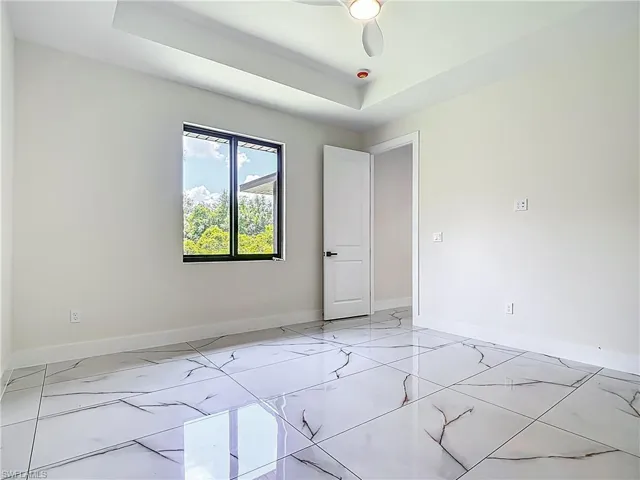 Unfurnished room with light marble finish floors, a tray ceiling, and a ceiling fan