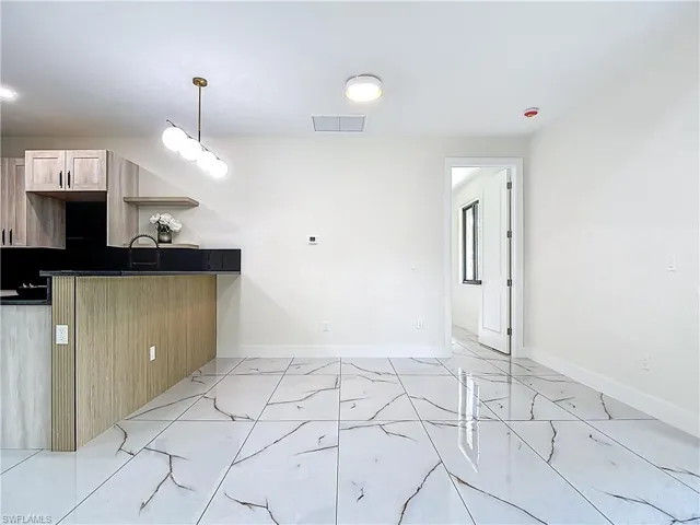 Dining area featuring light marble finish floors, dark countertops, light brown cabinetry, and hanging light fixtures