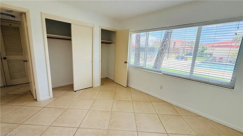Bright room featuring a wide window with horizontal blinds, neutral floor tile, and multiple closet spaces with bi-fold doors
