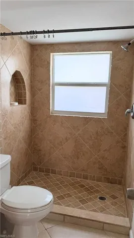 Walk-in shower featuring extensive neutral-toned diagonal tilework, an integrated arched niche, and a window for natural light