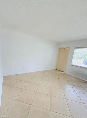 Spacious room featuring neutral tile flooring, white walls, and a light-colored entry door