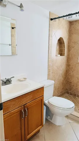Bathroom featuring a tiled shower with an arched niche, a single vanity with wood-finish cabinetry, and neutral-toned floor tile