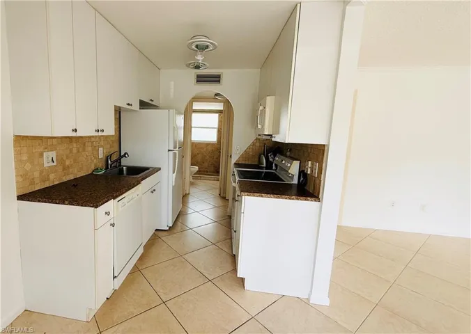 Galley-style kitchen featuring white cabinetry, granite-finish countertops, a tile backsplash, and a ceramic tile floor