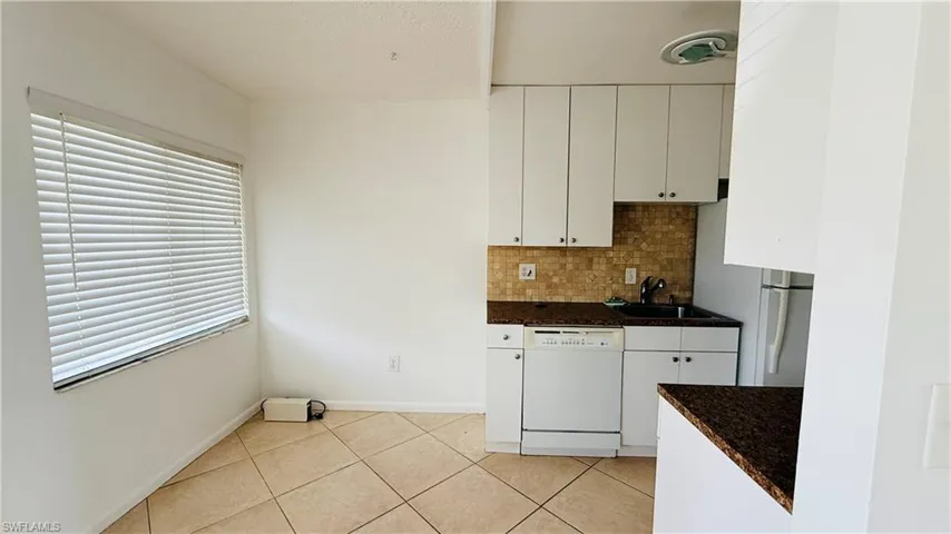 Kitchen space featuring white cabinetry, dark speckled countertops, and a tiled backsplash