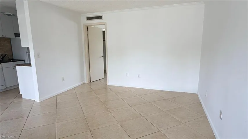 Spacious living area featuring tile flooring, white walls, and crown molding