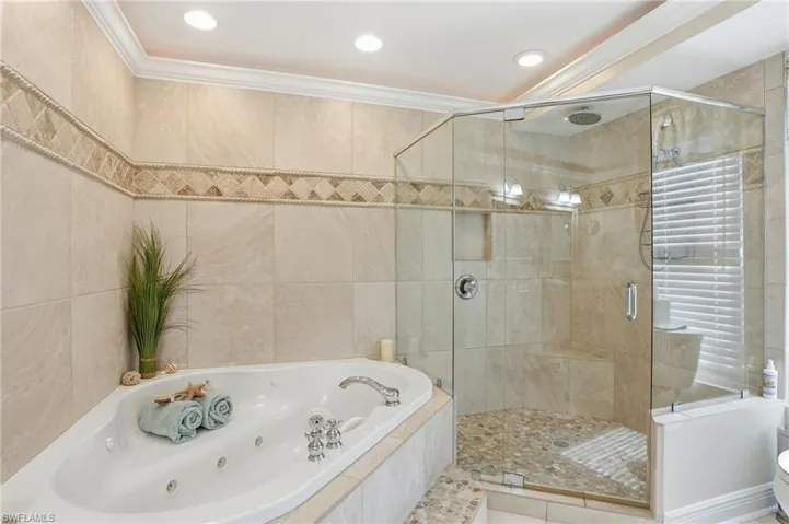 Bathroom with a whirlpool tub, a stall shower, tile walls, and ornamental molding