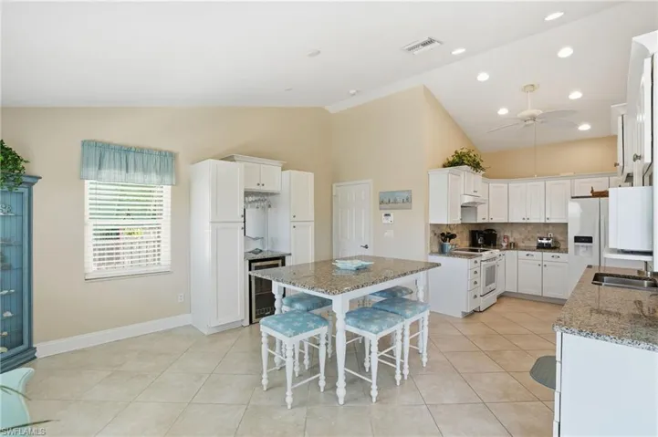 Kitchen featuring white cabinetry, a breakfast bar area, a ceiling fan, decorative backsplash, and lofted ceiling