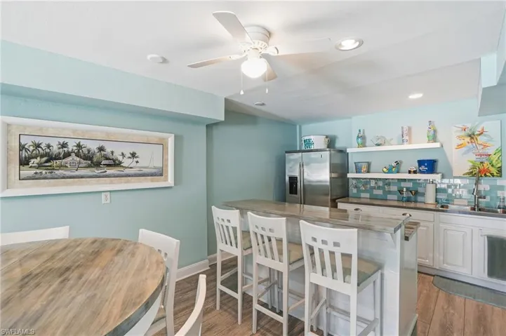 Kitchen with stainless steel fridge with ice dispenser, dark wood-style flooring, ceiling fan, a breakfast bar area, and white cabinets