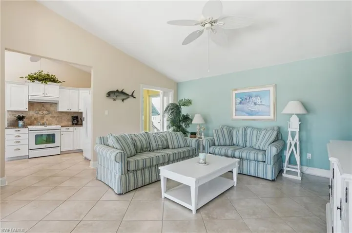 Living room with a ceiling fan, light tile patterned flooring, and lofted ceiling