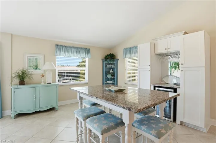 Kitchen with a breakfast bar area, dark stone countertops, beverage cooler, white cabinetry, and a center island