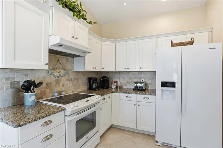 Kitchen with white appliances, white cabinetry, dark stone granite countertops, tasteful backsplash, and light tile patterned flooring