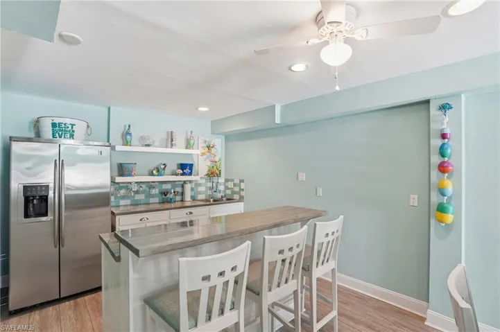 Kitchen featuring stainless steel fridge with ice dispenser, a kitchen breakfast bar, light wood-style flooring, a ceiling fan, and white cabinetry