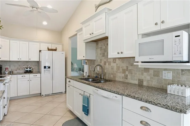 Kitchen with white appliances, white cabinetry, dark stone counters, a ceiling fan, and backsplash