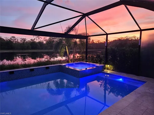 Pool at dusk featuring a lanai, a pool with connected hot tub, and a water view