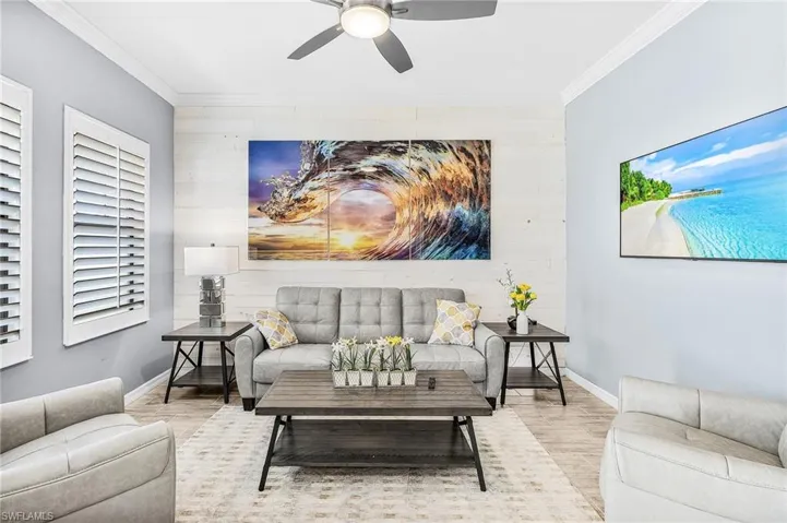 Living area featuring wood finished floors, wooden walls, a ceiling fan, ornamental molding, and an accent wall