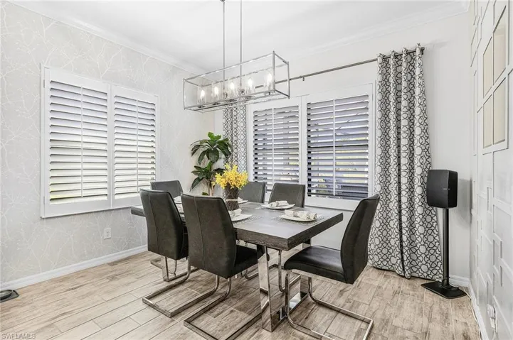 Dining area featuring wood finished floors, a chandelier, crown molding, and wallpapered walls