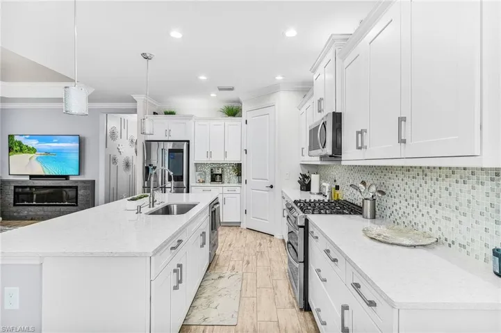 Kitchen featuring appliances with stainless steel finishes, crown molding, white cabinets, backsplash, and an island with sink