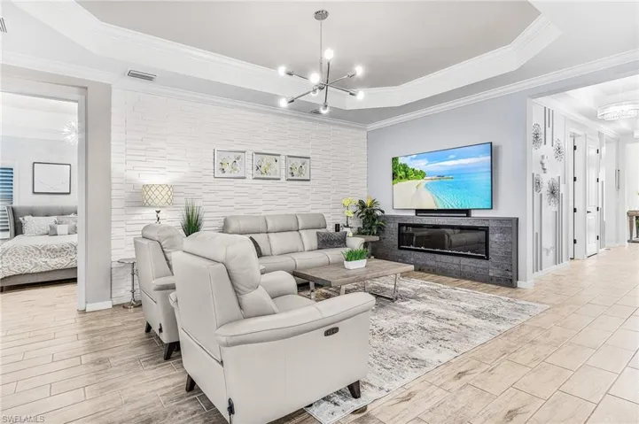 Living room with a raised ceiling, a chandelier, wood finish floors, and ornamental molding