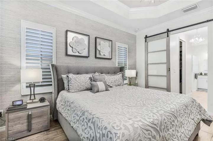 Bedroom with a barn door, a chandelier, a tray ceiling, crown molding, and wood finished floors