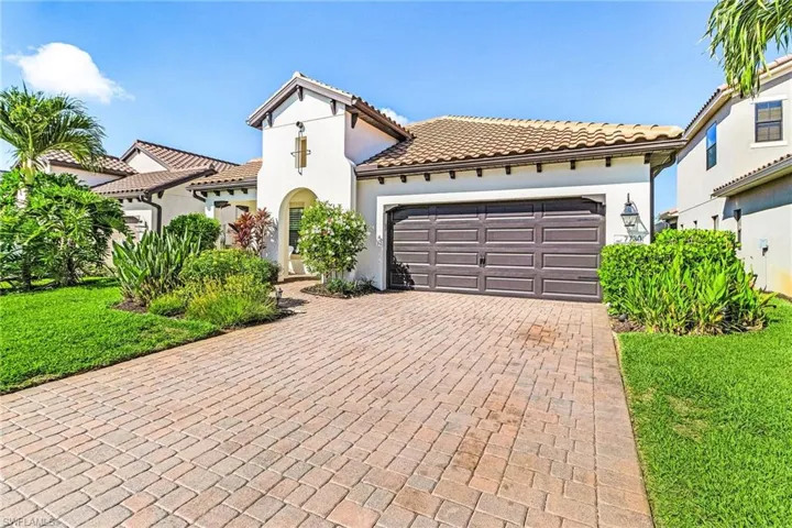 Mediterranean / spanish house with an attached garage, decorative driveway, a tiled roof, stucco siding, and a front lawn