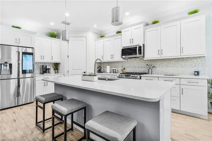 Kitchen featuring appliances with stainless steel finishes, white cabinetry, a kitchen bar, tasteful backsplash, and hanging light fixtures