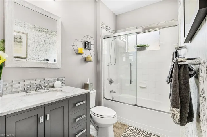 Bathroom featuring vanity, shower / bath combination with glass door, wood finished floors, and tasteful backsplash