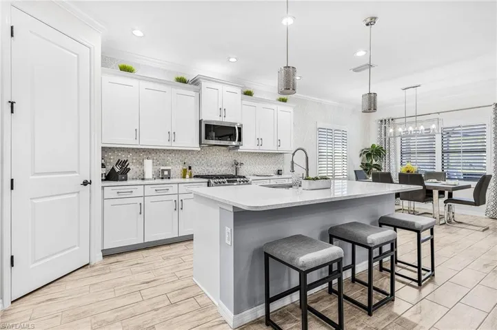 Kitchen featuring stainless steel microwave, a kitchen breakfast bar, light countertops, white cabinets, and decorative backsplash