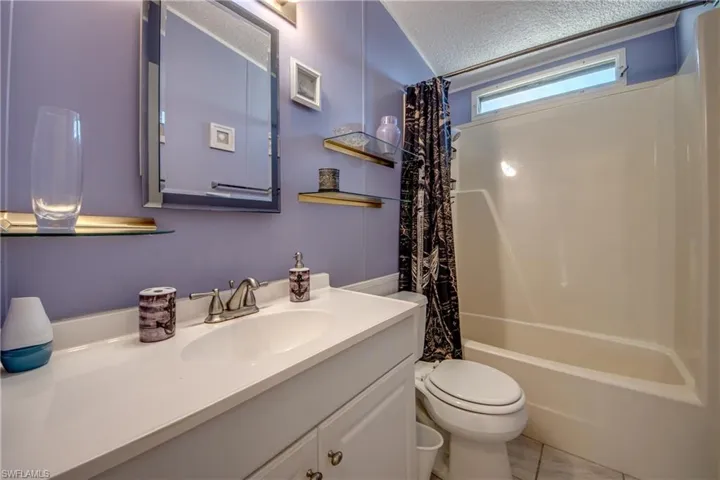 Full bathroom with vanity, a textured ceiling, toilet, and shower / bath combo with shower curtain