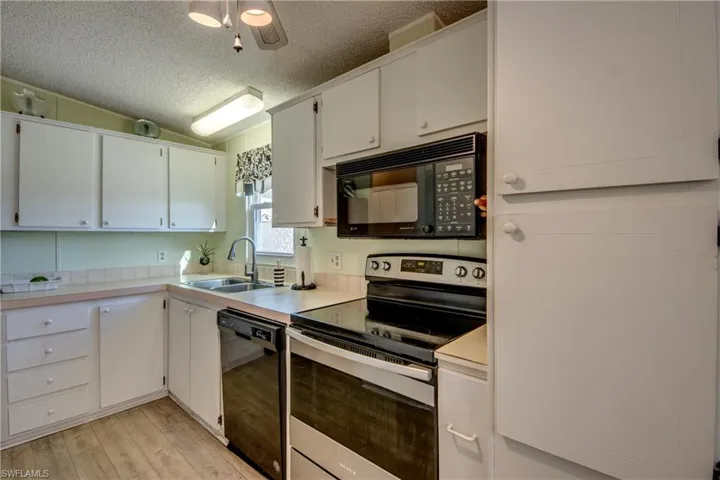 Kitchen with sink, light hardwood / wood-style floors, white cabinetry, and black appliances